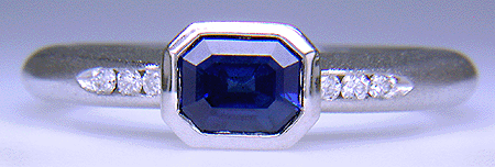 Emerald-cut sapphire set with round brilliant-cut diamonds in a custom platinum ring.