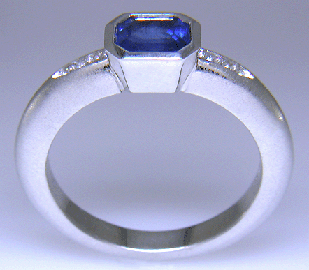 Side view of emerald-cut sapphire set with round brilliant-cut diamonds in a custom platinum ring.