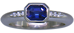 Emerald-cut sapphire set with round brilliant-cut diamonds in a custom platinum ring.