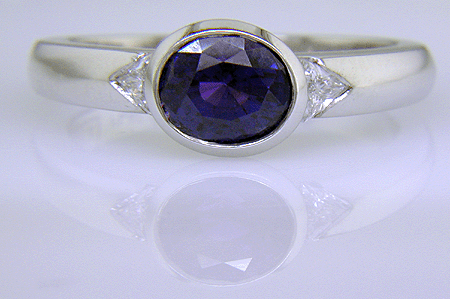 Oval sapphire ring with trilliant diamonds crafted in platinum.
