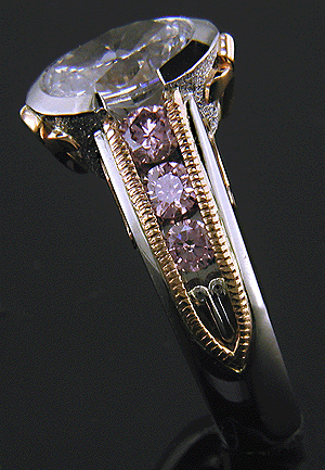 Shoulder view of oval diamond set with 6 brilliant pink diamonds in a custom rose gold and platinum ring.