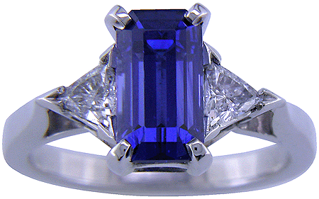 A handcrafted platinum ring with a sriking emerald-cut sapphire and two sparkling trilliant diamonds.