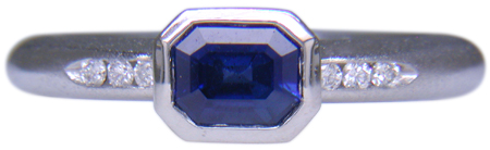 Emerald-cut sapphire set with round brilliant-cut diamonds in a custom platinum ring. (J6398)