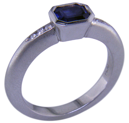 Emerald-cut sapphire set with round brilliant-cut diamonds in a custom platinum ring. (J6398)