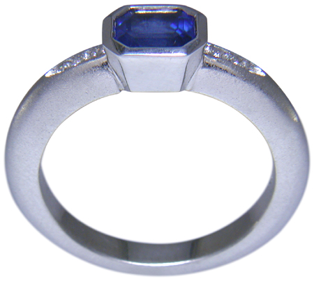 Side view of emerald-cut sapphire set with round brilliant-cut diamonds in a custom platinum ring. (J6398)