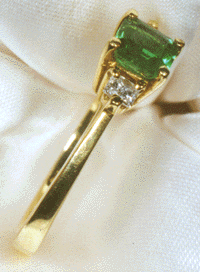 Side-view of 18kt gold ring with an emerald and princess cut diamonds.